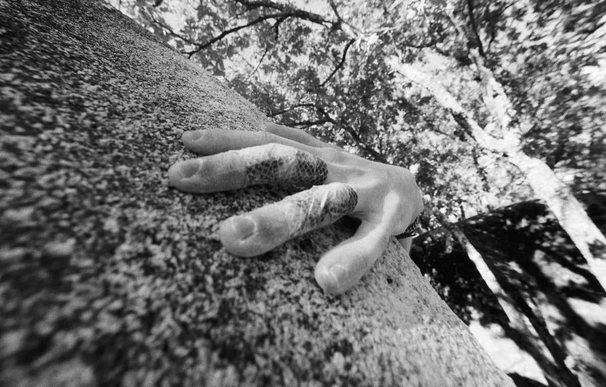 Una mano sobre el canto de un bloque de granito, con los árboles al fondo.